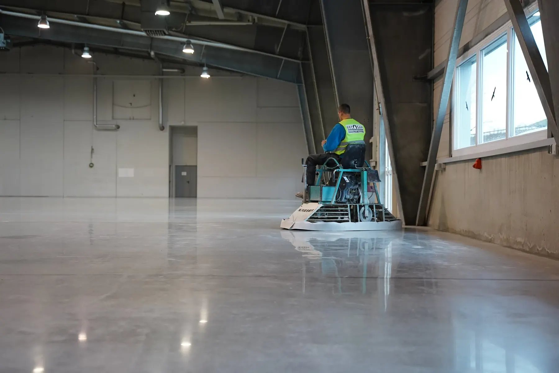 A crew member operating a ride-on machine on a polished concrete floor in a large building
