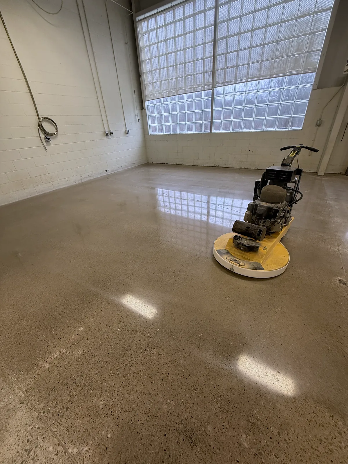 A walk-behind floor burnisher on a polished concrete floor in a room with a glass block window, Pittsburgh area.