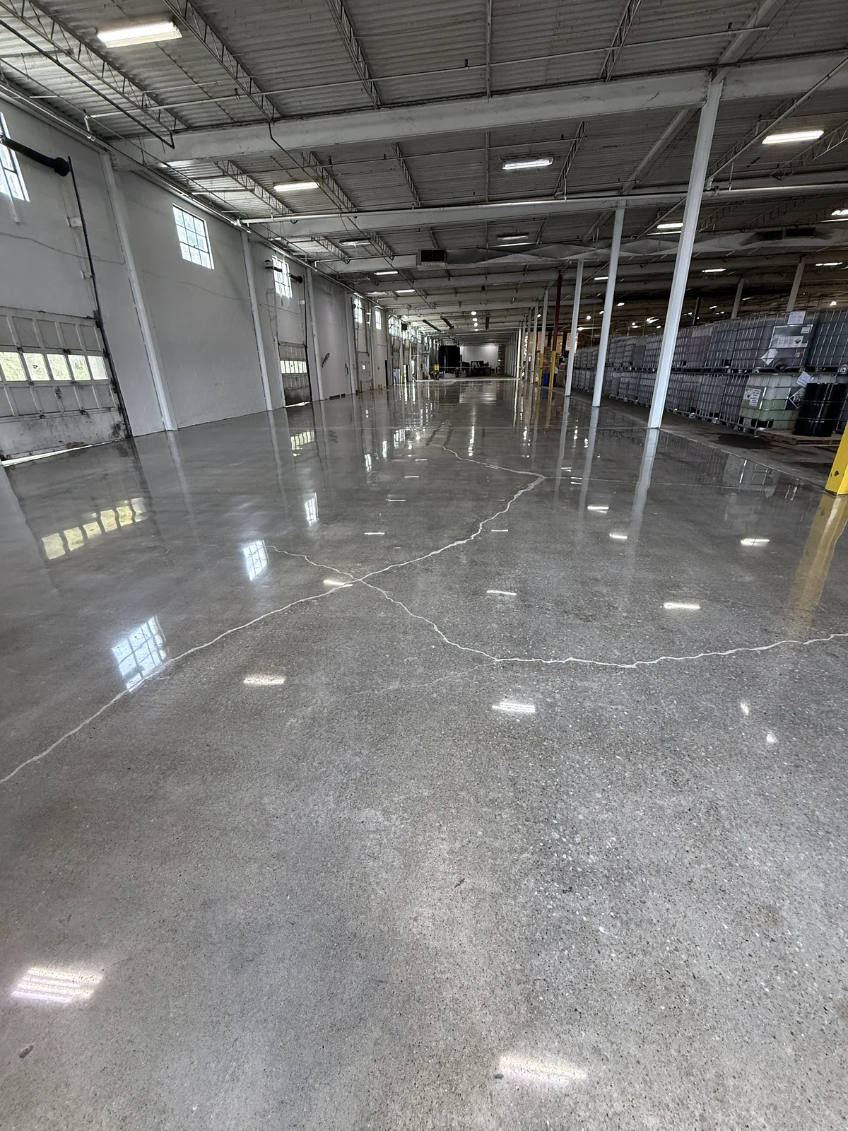 Industrial bay with overhead dock doors and steel columns, polished concrete floor with a hairline crack, Pittsburgh area.