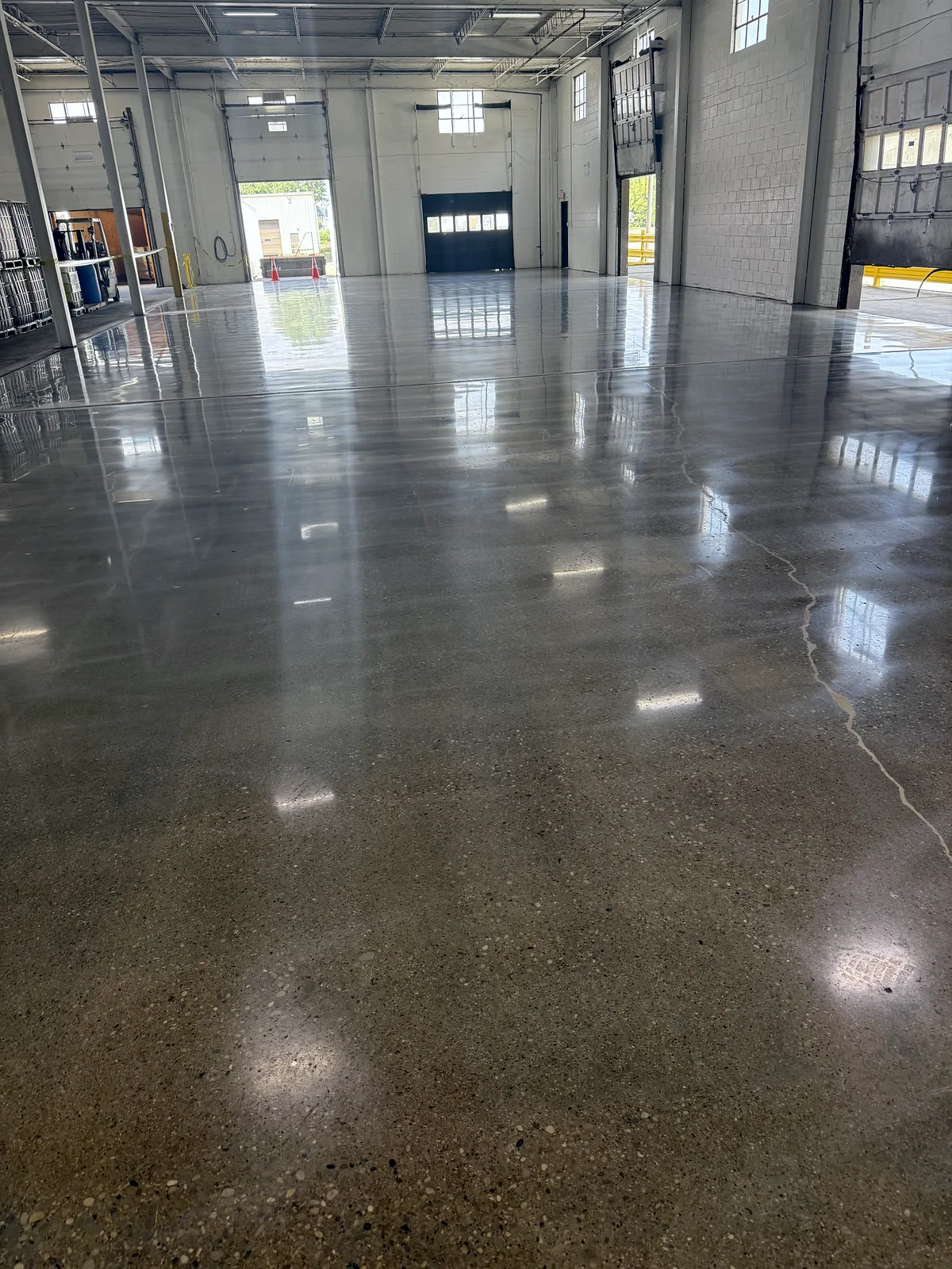 Industrial bay with dock doors, dark glossy polished concrete floor and a hairline crack, Pittsburgh area.