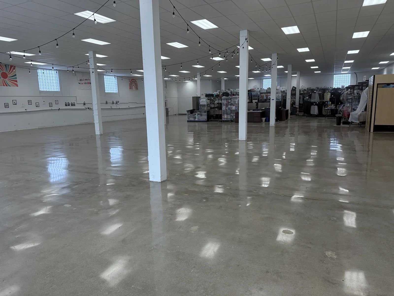 Open commercial room with white support columns and string lights, polished concrete floor with light reflections, Pittsburgh area.