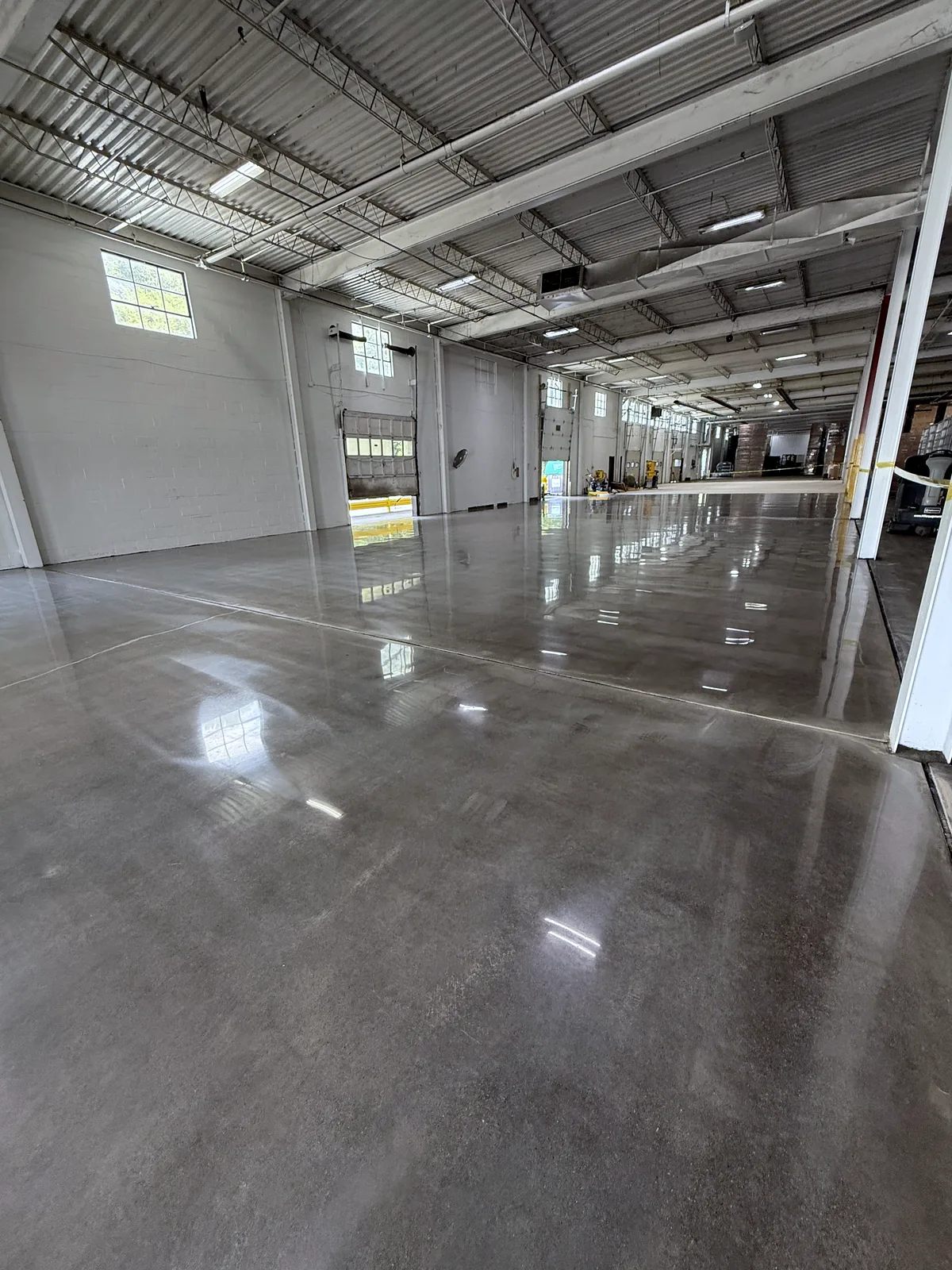 Industrial bay with steel roof trusses and a high window, glossy polished concrete floor reflecting the lights, Pittsburgh area.