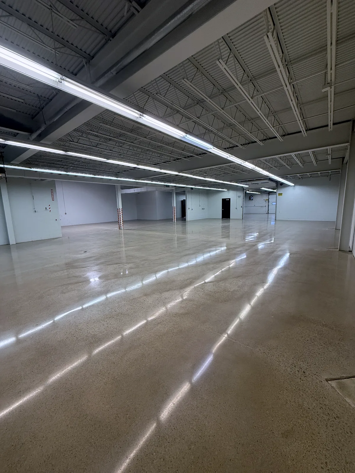 Large empty warehouse with long fluorescent tubes overhead reflected in a polished concrete floor, Pittsburgh area.